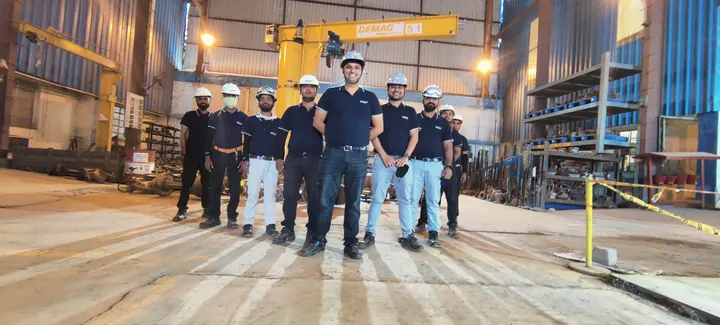 Shop-floor team of Venus Engineering Works in branded polo shirts and white hard hats, lined up under the overhead crane at the Kuha works.